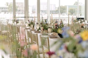 Elegant wedding reception table setting with gold chairs and soft floral centerpieces in bright natural light.