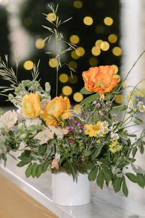 Beautiful floral arrangement with orange and yellow roses in a white vase against a bokeh background with golden lights.