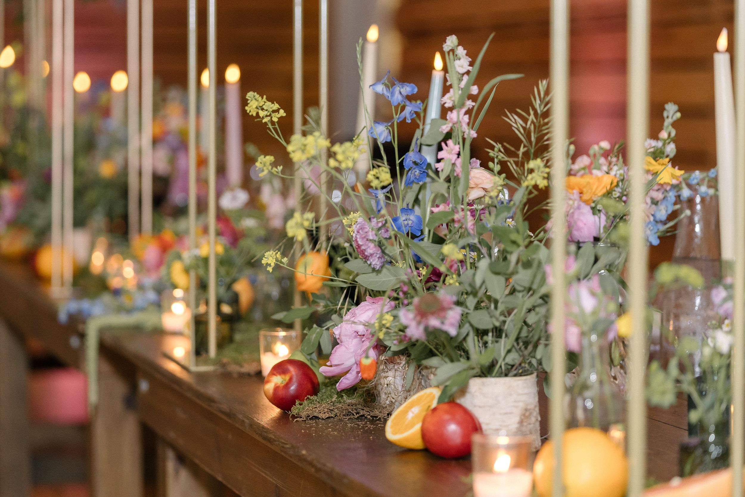 Elegant table arrangement with candles and wildflower centerpieces featuring peaches and colorful blooms in glass vases.