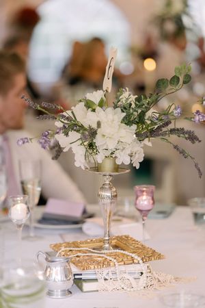Elegant wedding table centerpieces feature white flowers in crystal vases alongside golden wicker charger plates.