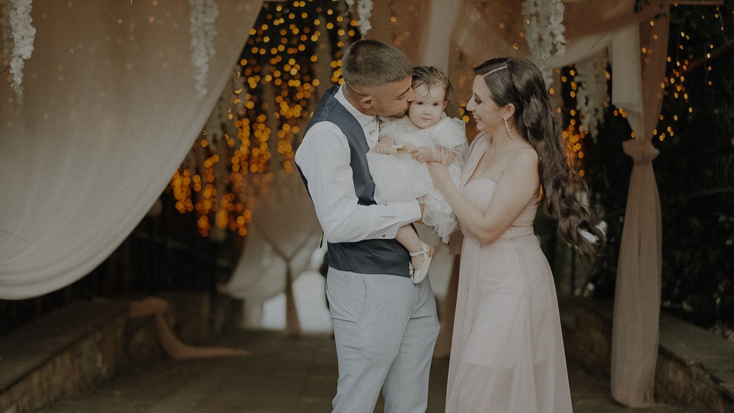 A romantic dance moment under twinkling lights and draped fabric at an evening celebration.
