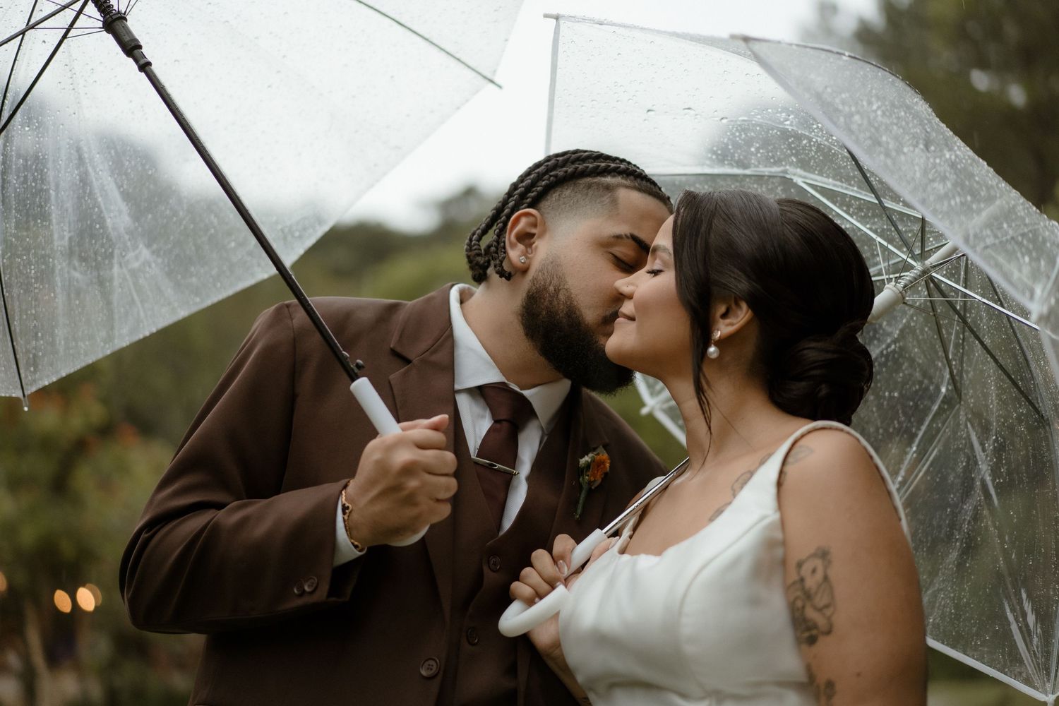 A romantic moment shared under clear umbrellas during a rainy wedding photoshoot.