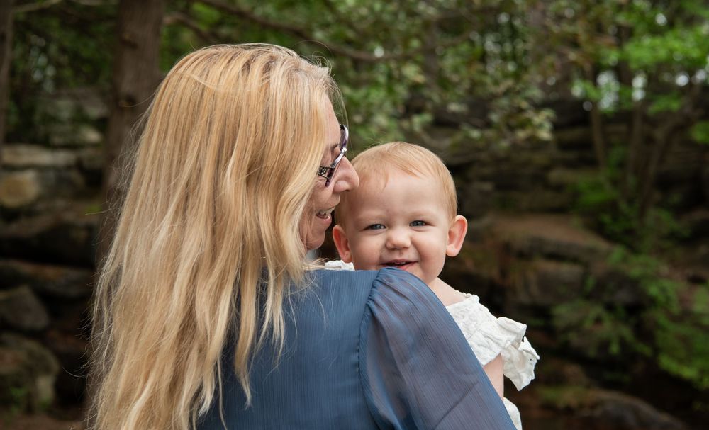 An intimate outdoor moment between parent and baby, surrounded by lush green foliage and stone walls.