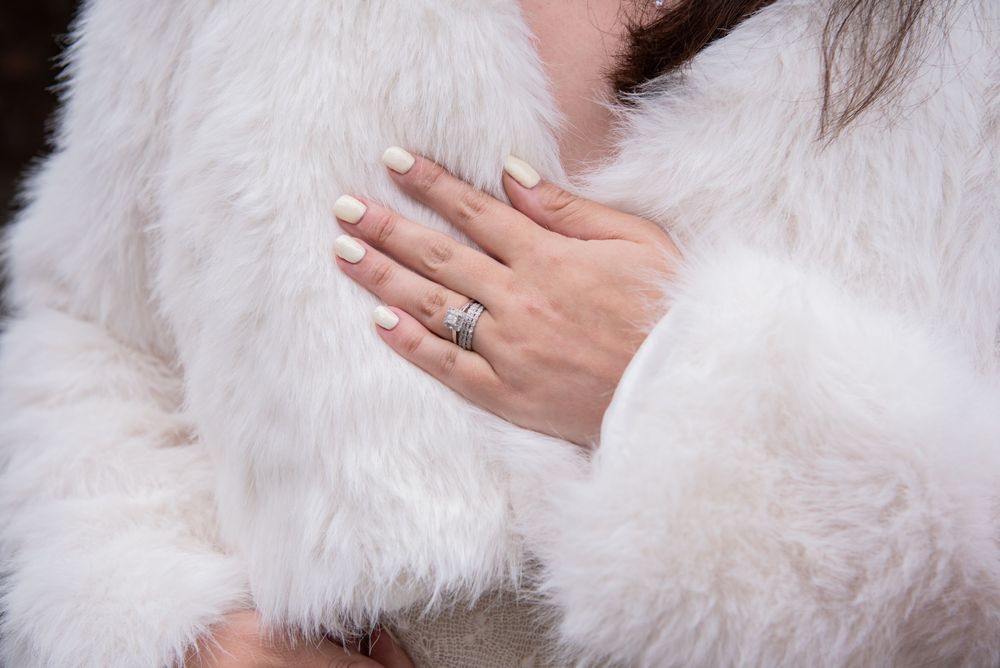 Close-up of engagement ring on hand against white fur coat background.