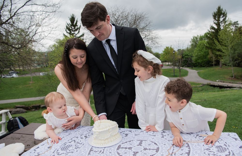 A family gathers around a white tablecloth outdoors to sign or view a document together.