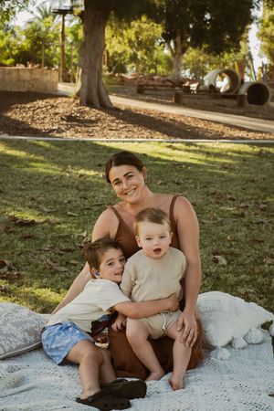 A casual family moment captured on a white blanket under shady trees in a park.