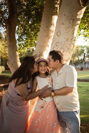 A family shares tender moments together in a sun-dappled park setting during golden hour.