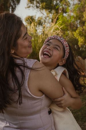 Two friends share a joyful moment laughing together outdoors in natural lighting among trees and foliage.