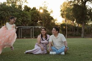 A couple sits together on a grassy lawn during golden hour sunset while enjoying a picnic spread.