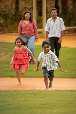 Family members run and jump together on a grassy field in coordinated outfits during a playful outdoor photo session.