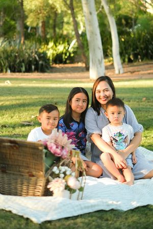 A group enjoying a sunny picnic on a white blanket in a grassy park with wicker baskets nearby.