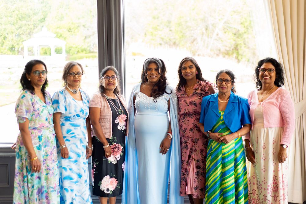 A group of women stand together smiling in colorful floral and patterned dresses at a formal event.