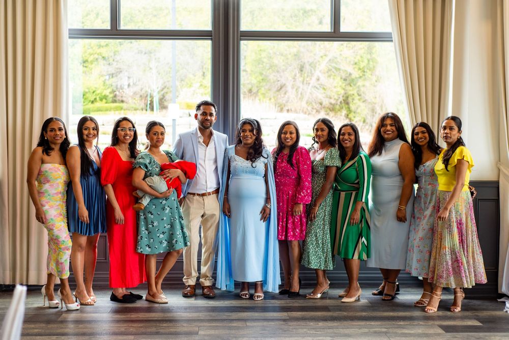 A group stands by a window wearing colorful formal dresses and outfits in shades of blue, pink, green, and yellow.