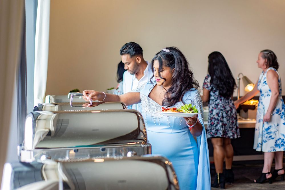 People serving themselves food from stainless steel chafing dishes at a buffet-style event.