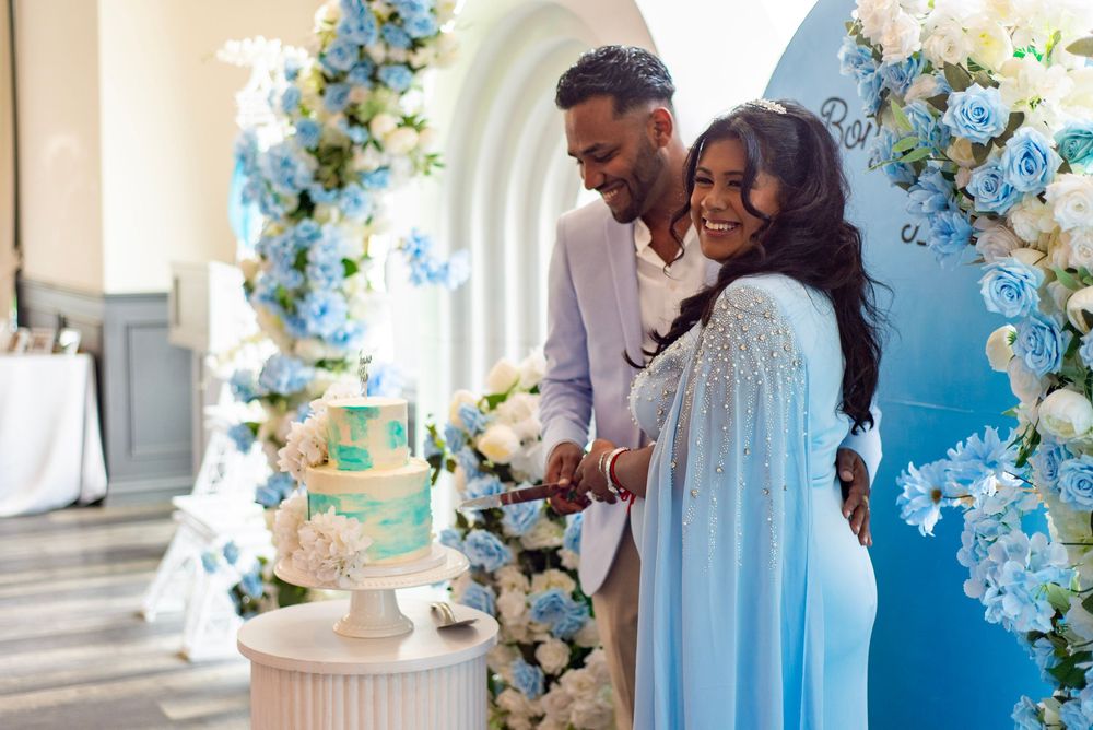 A couple shares a joyful moment while cutting their wedding cake surrounded by blue and white floral decorations.