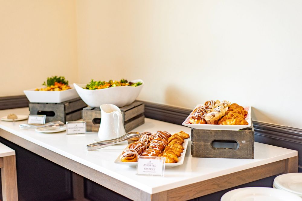 A buffet table setup with wooden serving trays containing pastries and food warmers for catering service.