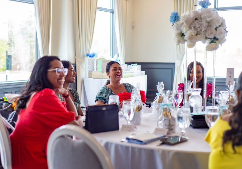 People enjoying a social gathering at decorated tables with floral centerpieces by sunlit windows.