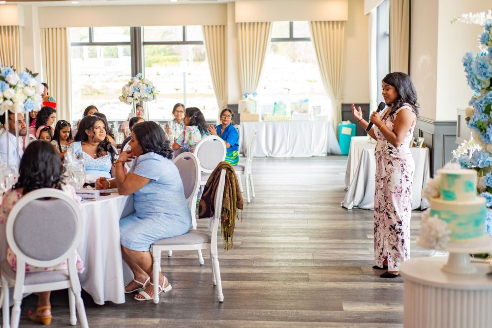 Event guests seated at round tables in an elegant venue with white decor while a speaker addresses the gathering.