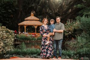 Family portrait in garden setting with gazebo and lush greenery in background.