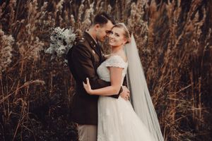 Romantic autumn wedding portrait with couple embracing among tall grasses at sunset.