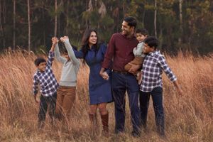 Family enjoying playful moment together in tall grass field during golden hour.