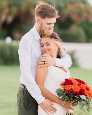 Intimate wedding portrait with couple embracing while holding colorful red and orange bouquet.