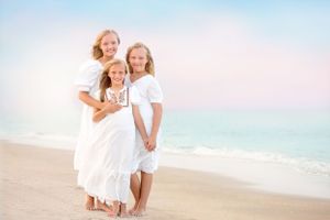 Three people in white outfits sharing a tender moment on the beach.