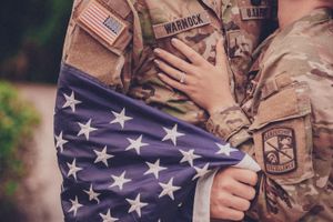 Military uniform with American flag detail and hands showing wedding rings.