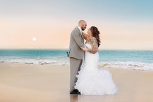 A romantic beach wedding photo of a couple embracing at sunset with waves in the background.