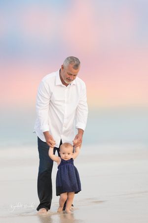 Adult and young child walking hand in hand along the beach at sunset.