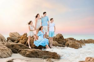Family group in coordinating blue and white outfits posing on beach rocks.