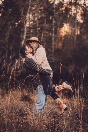 Couple embracing in autumn forest with dog jumping beside them at golden hour.