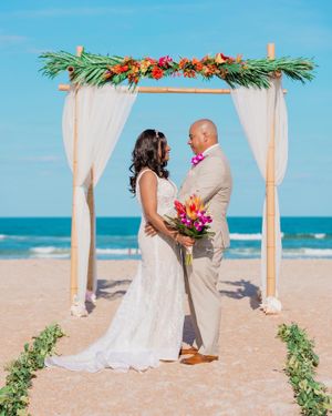 Beach wedding ceremony under floral arch with ocean backdrop.
