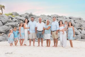 Large family group poses for portrait on rocky beach wearing coordinated blue and white outfits.