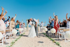 Beach wedding celebration with guests cheering on sandy shore.