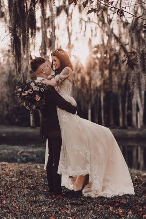A romantic wedding photo in a mossy forest with Spanish moss as newlyweds embrace at sunset.