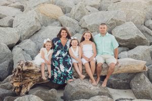 Family sitting together on rocky beach with ocean waves in background.