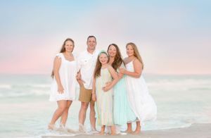 Family in white and pastel outfits posing together on beach at sunset.