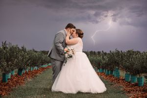 A dramatic wedding photo with lightning strike behind couple in an orchard.