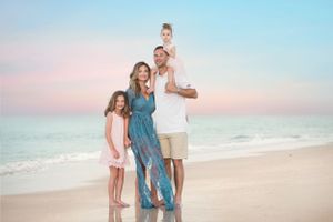 Family of four poses together on beach at sunset in coordinated blue and white outfits.