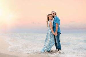 Couple in casual elegant attire embracing on beach during golden hour sunset.