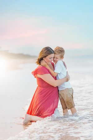 Tender moment between mother and child playing in ocean waves at sunset.