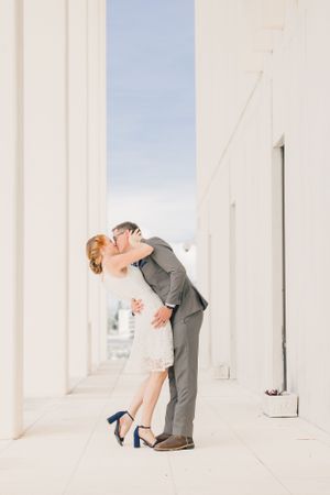A couple shares a romantic dip kiss in an elegant white corridor.