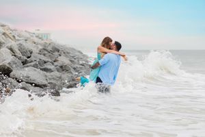 A romantic embrace in the crashing waves on a rocky beach at sunset.