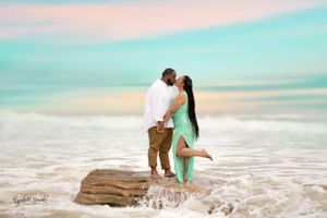 Romantic couple embracing on rocky outcrop with ocean waves splashing behind them.