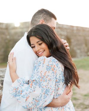 A couple shares a tender embrace outdoors, with one wearing a floral print dress.