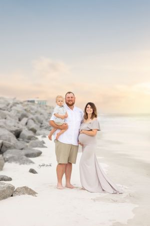 A beachside family portrait at sunset with rocky coastline in the background.