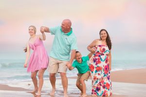 Family in colorful outfits playing and dancing together on beach at sunset.