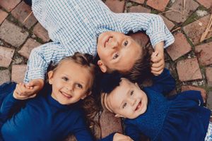 Three children lying on brick pavement smiling and laughing together.