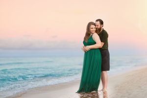 Romantic couple embraces on beach at sunset with waves and pink sky in background.
